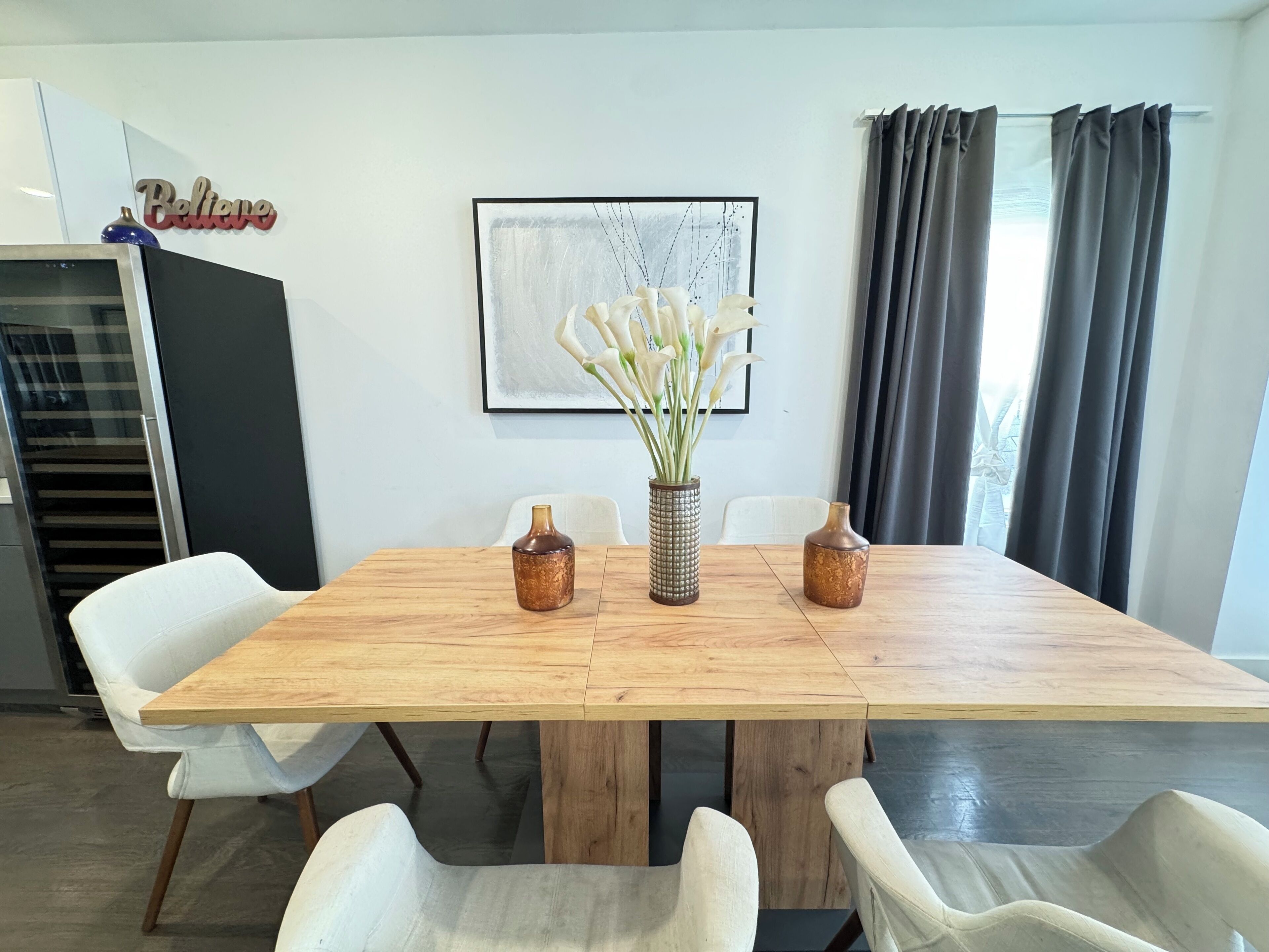 Un comedor con una mesa de madera, sillas blancas y tres jarrones decorativos.