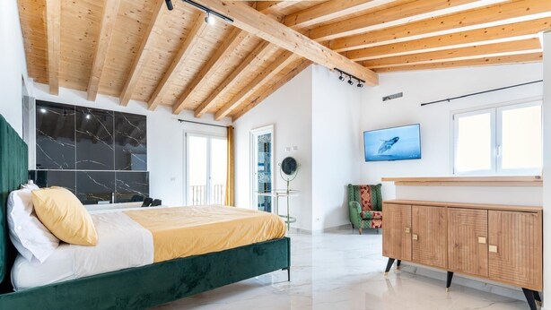 Quarto moderno com cama verde, teto de madeira, piso de mármore, televisão e cadeira verde.
