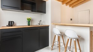 Cozinha moderna com armários pretos, bancada de madeira, cafeteira e dois bancos de bar brancos.