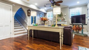 A living room with a wooden floor, a ceiling fan, a television, a sofa, and a staircase. - Charming 3-bedroom cottage in Oakleigh Historical District in downtown Mobile (Mobile)