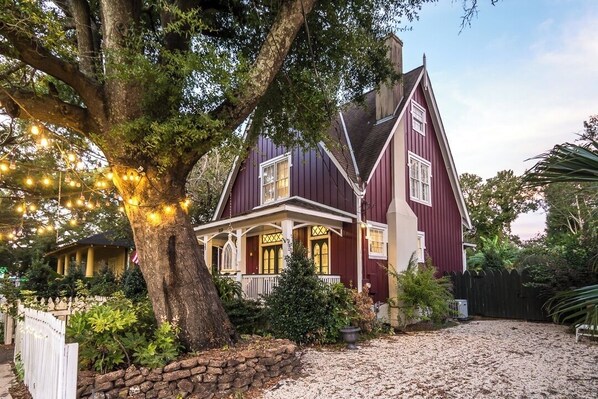 Une grande maison avec un arbre imposant devant, une clôture blanche en bois et une allée gravillonnée.