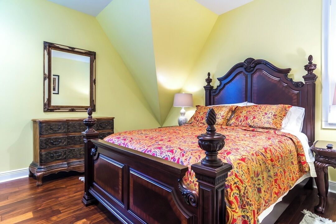 A bedroom with a wooden bed, a dresser, a mirror, and a lamp.