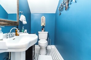 Une salle de bain avec un lavabo blanc, des toilettes et un miroir. Une serviette est accrochée au mur et un objet décoratif est placé au-dessus des toilettes.