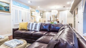 A living room with a brown leather sectional sofa, ottomans, and a dining area with a chandelier. - Charming 3-bedroom cottage in Oakleigh Historical District in downtown Mobile (Mobile)