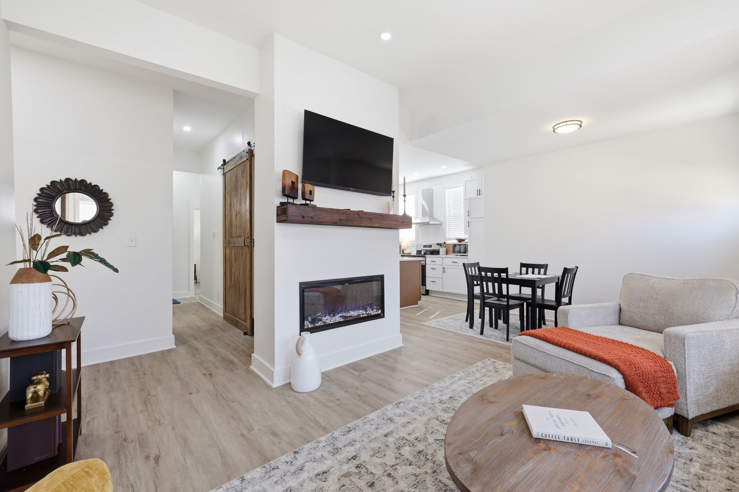 A modern living room with a fireplace, a dining area, and a kitchen in the background.