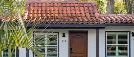 A single-story house with a red-tiled roof, a wooden door, and a number '118' on the front wall.
