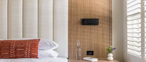 A modern bedroom with a large bed, a wooden headboard, a bedside table with a bottle, a book, and a vase.