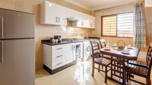A compact kitchen with a built-in oven, a refrigerator, and a dining area with a table and chairs.