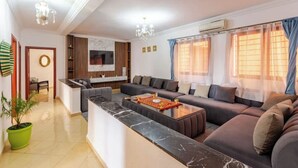 A modern living room with a sofa set, a marble coffee table, and a dining area with a kitchen in the background.