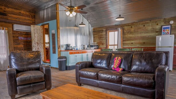 A rustic interior with leather sofas, a wooden coffee table, and a kitchen area with a refrigerator and sink. - Leaning Tower of Alpine (Alpine)