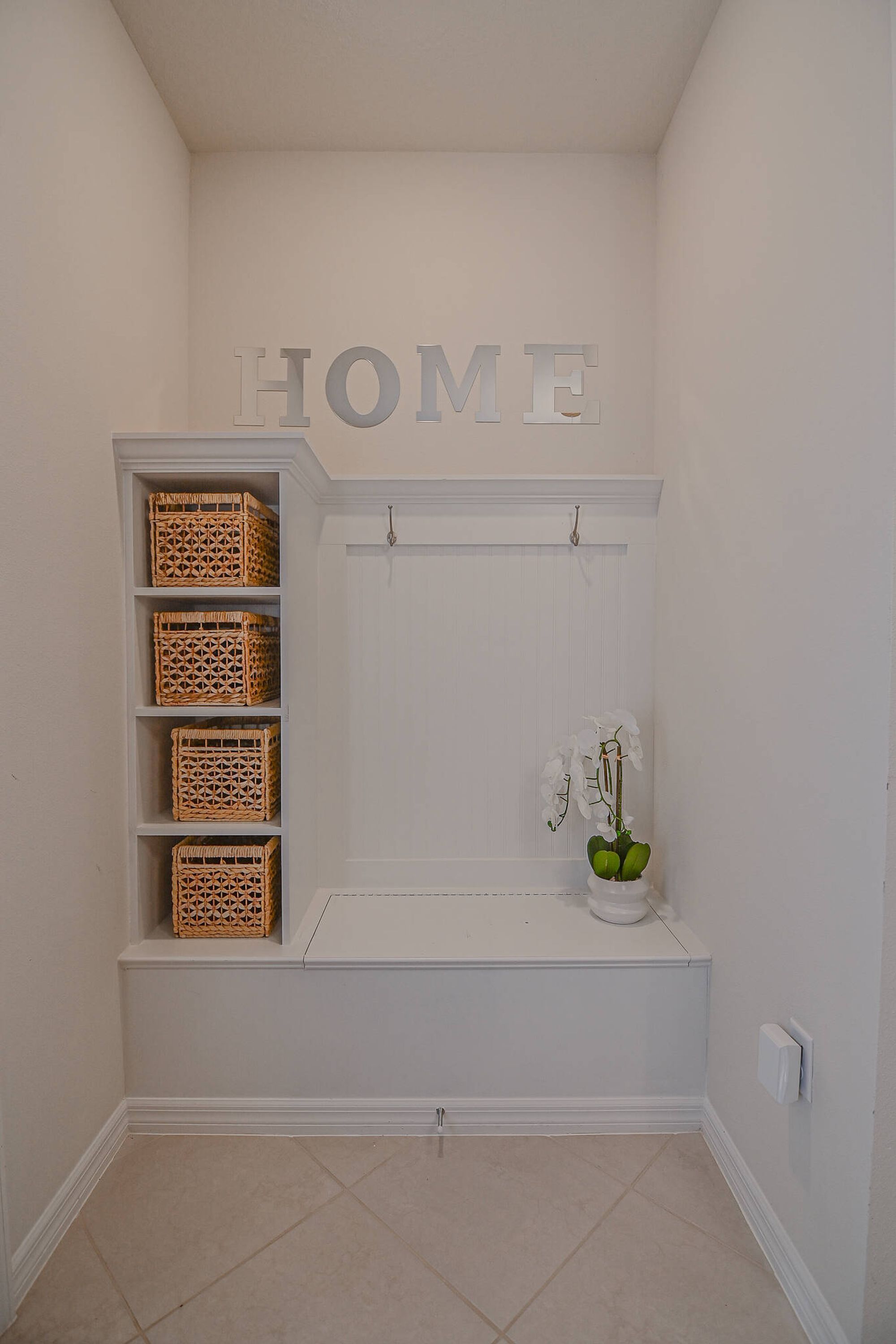 A white interior with a 'HOME' sign, wicker baskets on shelves, and a potted orchid.