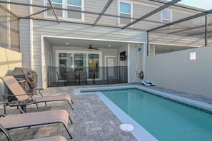 En swimmingpool med et glasindhegning, liggestole og en patio.