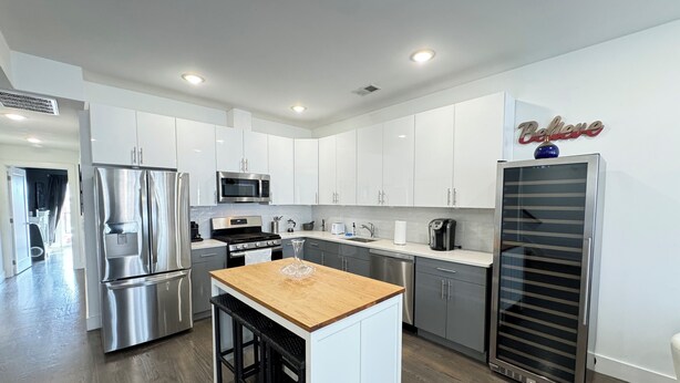 A modern kitchen with white cabinets, stainless steel appliances, and a wooden island. - ROOFTOP VIEWS OF NYC+FREE Parking+Washer&Dryer (Jersey City)