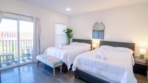 A hotel room with two beds, a bench, a small table, a potted plant, and a balcony with a view. - ROOFTOP VIEWS OF NYC+FREE Parking+Washer&Dryer (Jersey City)
