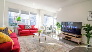 A modern living room with a red sofa, a coffee table, and a TV on a wooden stand. - ROOFTOP VIEWS OF NYC+FREE Parking+Washer&Dryer (Jersey City)