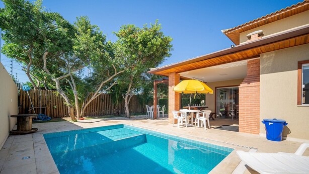 Un patio trasero con piscina, mobiliario de exterior y un área de estar cubierta.