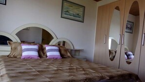 Une chambre à coucher avec un grand lit, deux oreillers, une tête de lit, une armoire et un tableau encadré accroché au mur.