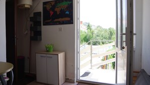 Une pièce dotée d’une porte-fenêtre coulissante donnant sur un balcon, d’une carte du monde accrochée au mur et d’une petite armoire contenant une plante en pot.