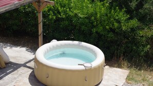 Un jacuzzi rond, surmonté d’une structure en bois et entouré de verdure.