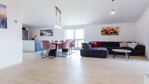 A spacious living area with a dining table and chairs, a sofa, and a kitchen in the background.