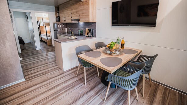 A modern kitchen with wooden cabinets, a built-in microwave, and a large flat-screen TV mounted on the wall.