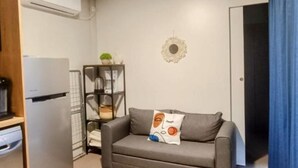 A compact living space with a grey sofa, a small side table, a white wall decoration, and a door with a blue curtain. - SAK Mobile Homes - Standard Two Bedroom Mobile Home with Terrace and Sea View (Pirovac)