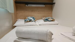 A neatly made bed with white linens and a rolled towel, two decorative pillows with tropical patterns, and a wooden headboard with a light fixture. - SAK Mobile Homes - Standard Two Bedroom Mobile Home with Terrace and Sea View (Pirovac)