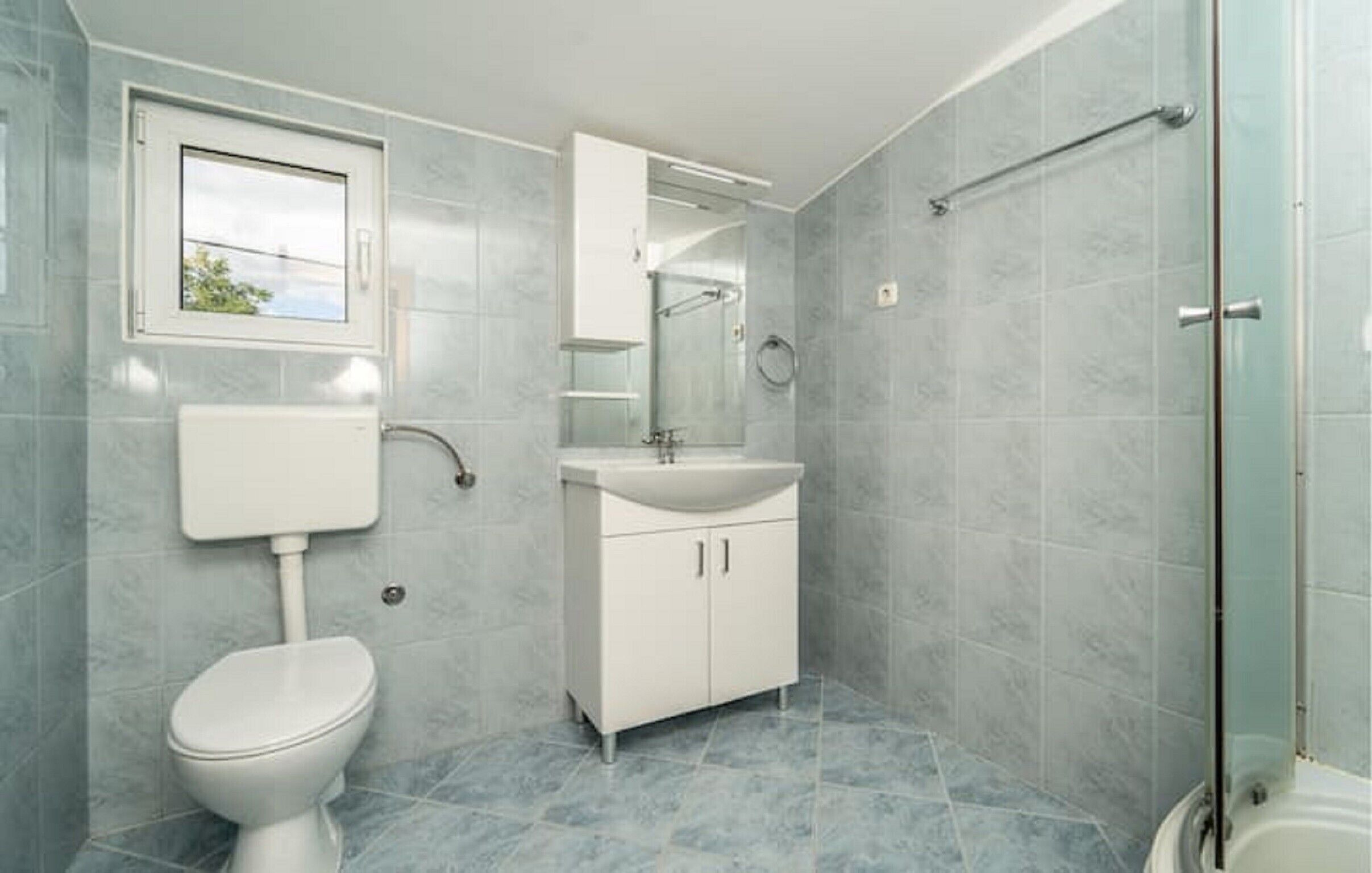 Ein Badezimmer mit Toilette, Waschbecken, Spiegel und Duschbereich.