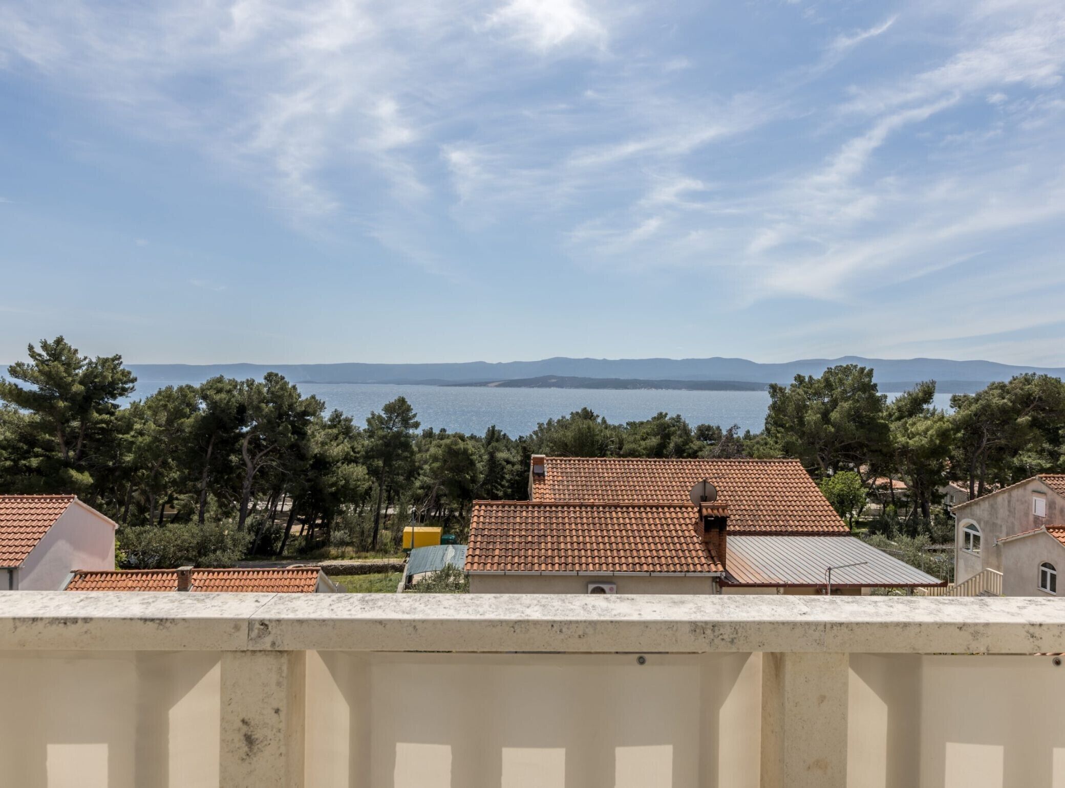 Una zona residencial costera con casas de tejados de terracota, cielo despejado y vistas al mar y montañas distantes.