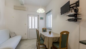 A compact living space with a white sofa, a dining table with four chairs, a TV mounted on the wall, and a ceiling fan. - Adriatic Island Sea View -Cmfrt 1Bedroom/TerraceA2 (Bol)