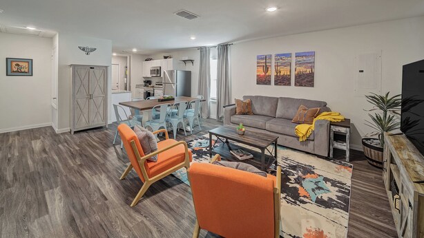 A modern living room with a dining area, a gray sofa, orange chairs, and a kitchen in the background.