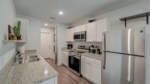 A modern kitchen with white cabinets, stainless steel appliances, granite countertops, and a wooden floor.