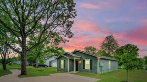 A single-story house with a green exterior, a front porch, and a driveway leading to the entrance.