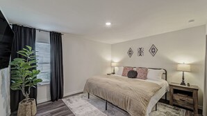 A bedroom with a bed, bedside tables, a potted plant, and decorative wall art.