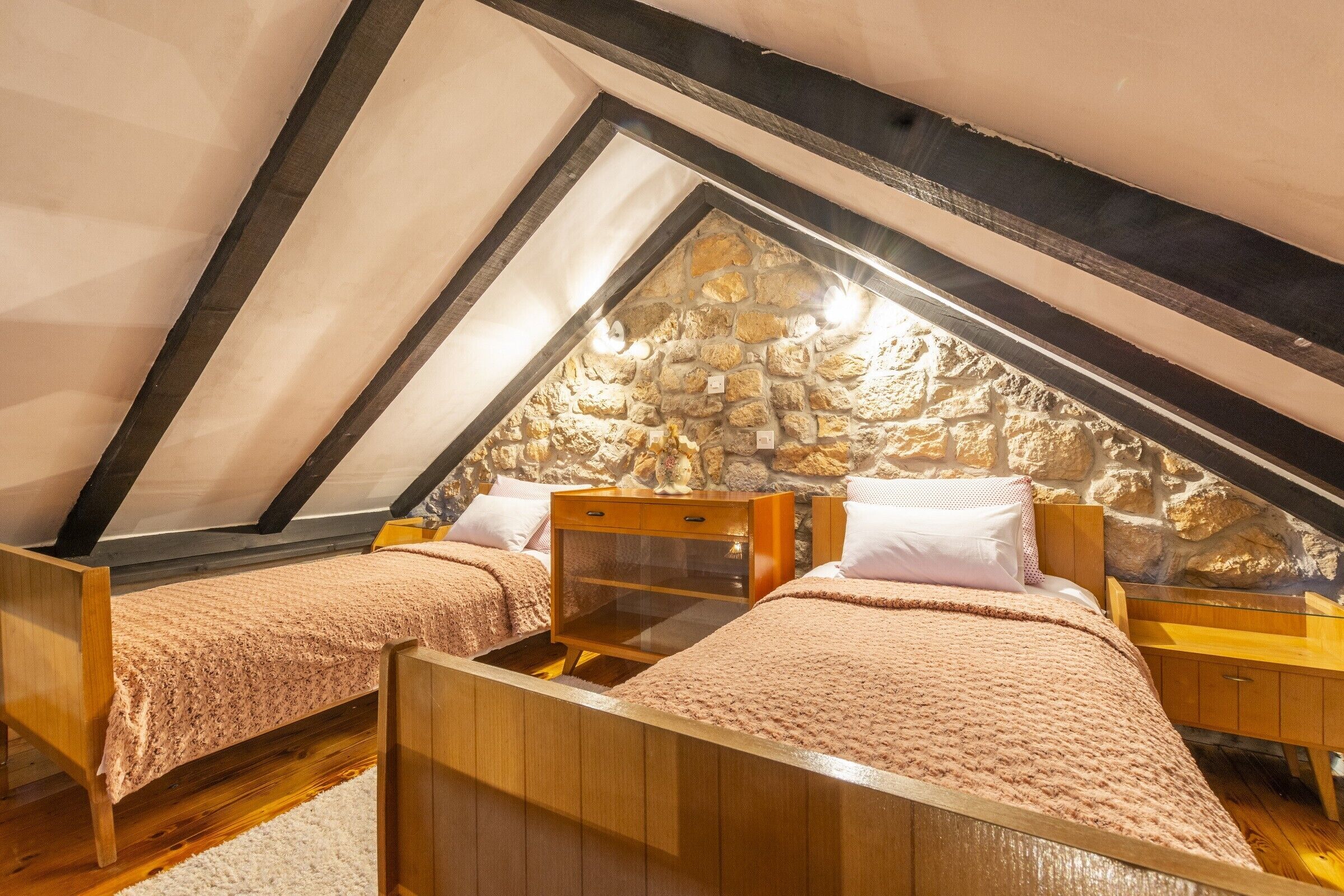 A cozy attic bedroom with two wooden beds, a stone wall, and a sloped ceiling.