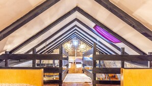 A cozy attic bedroom with a sloped ceiling, wooden beams, and a stone wall in the background.