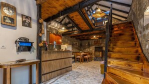 A rustic interior with a wooden staircase, stone floor, and a bar area with wooden furniture.