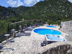 A pool area with two hot tubs and lounge chairs, surrounded by stone flooring and a mountainous backdrop. - Rustical Resort Kokorići/Shared Pool - One Bedroom (Vrgorac)