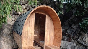 A wooden sauna with a curved roof, built into a stone wall, and featuring a bench and steps inside.