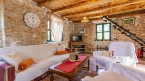 A cozy living room with stone walls, wooden beams, a clock, a sofa, a coffee table, and a staircase.