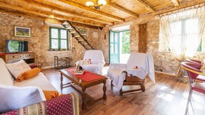 A rustic wooden interior with stone walls, a wooden staircase, a television, and a dining area with chairs and a table.