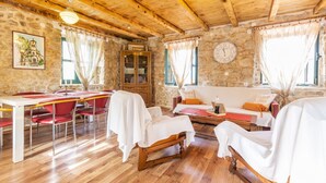 A rustic room with a wooden ceiling, stone walls, a dining table with chairs, a sofa, and a clock on the wall.