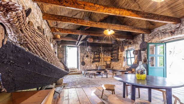 Un intérieur rustique avec des murs en pierre, des poutres en bois, une table ronde et une cheminée en pierre.