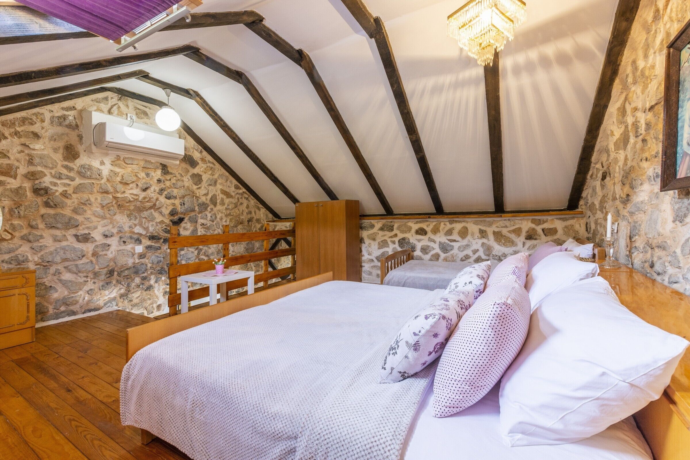 Une chambre avec un mur en pierre, des poutres apparentes, un lit avec une literie blanche, une chaise en bois et une petite table.