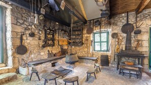 Une cuisine rustique en pierre, dotée d’un grand foyer, de tabourets en bois et de divers ustensiles de cuisine.