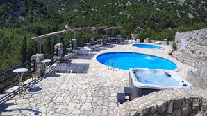 Un espace piscine doté de deux bains à remous et de chaises longues, entouré d’un sol en pierre et offrant une vue imprenable sur les montagnes.
