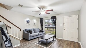 A living room with a grey sofa, a dark coffee table, and a ceiling fan. - Cowboy Oasis !King Bed with WiFi by Domain (Austin)