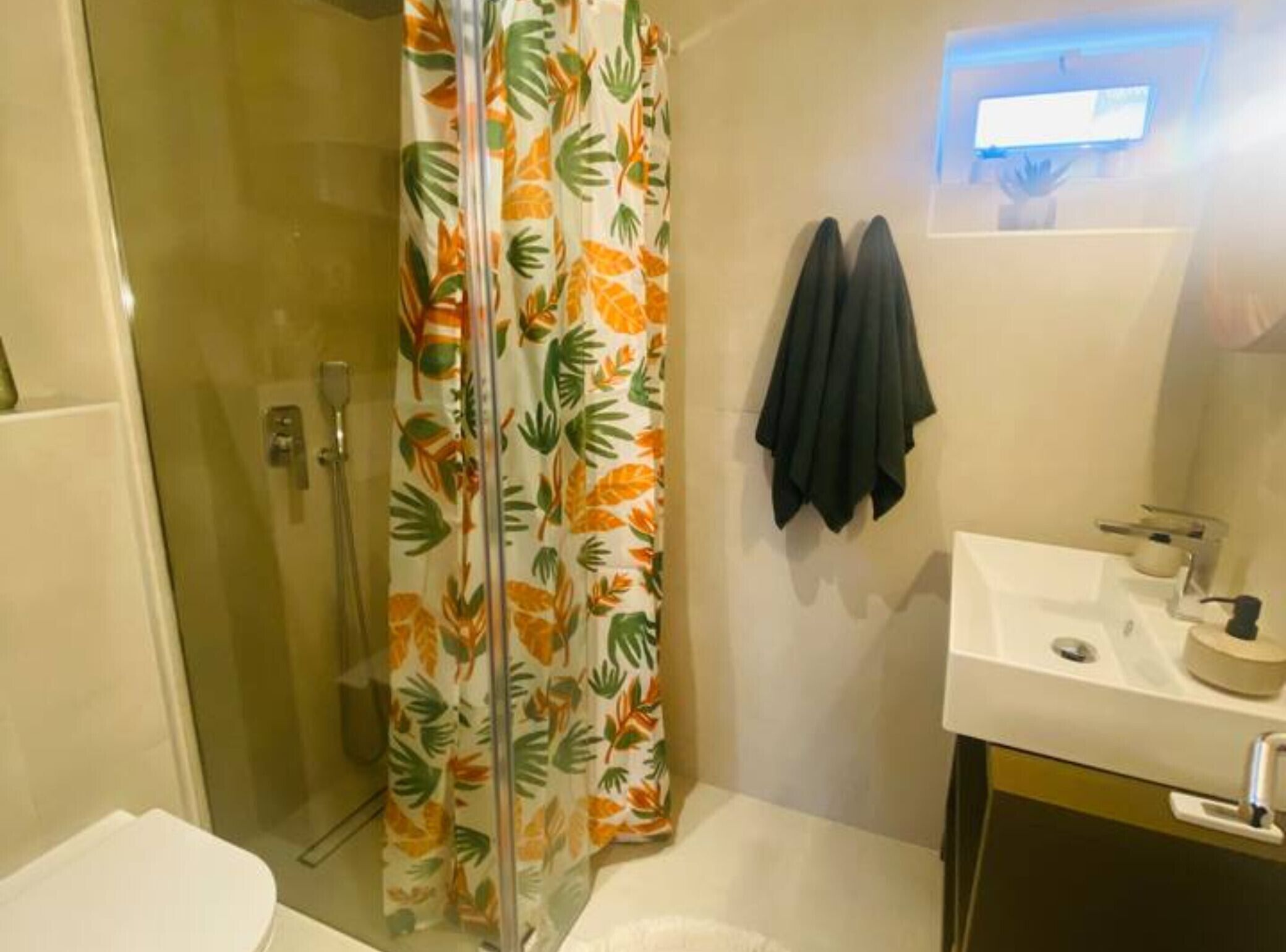 A bathroom with a shower, toilet, sink, and a towel hanging on the wall.