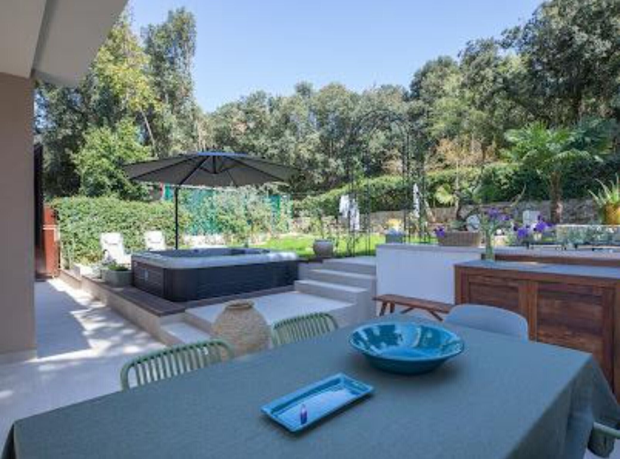 Een terras buiten met een tafel, stoelen, een jacuzzi en een grote parasol.