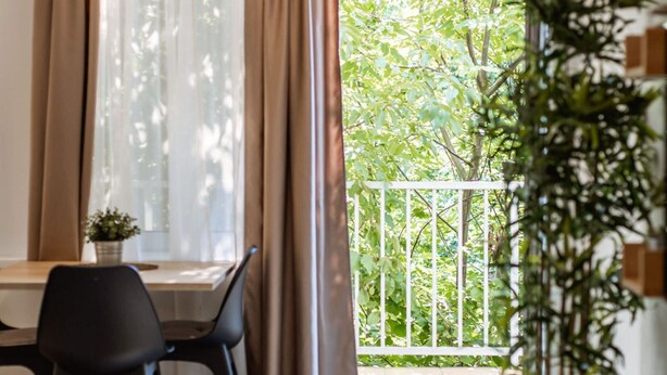 A room with a dining table, chairs, a potted plant, and a view of a balcony with greenery. - Stylish Apartments with Osijek - Standard Studio (Osijek)